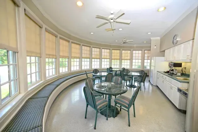 Bright sunroom dining area with curved bench seating, table and chairs, large windows, and kitchen counter.
