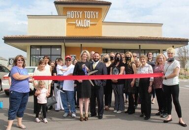 People cutting a ribbon in front of the Hotsy Totsy Salon, opening celebration.