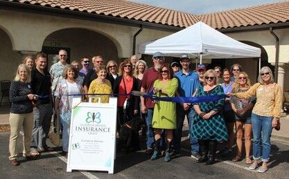 Group of people at a ribbon-cutting ceremony for an insurance business, in front of a building.