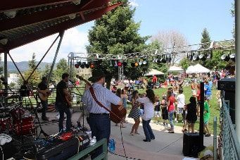 Band playing on stage at outdoor festival; people dancing on the lawn.