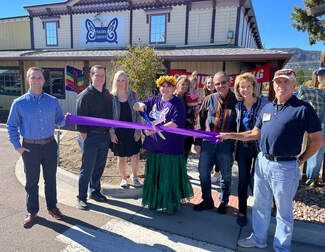 People at a ribbon-cutting ceremony in front of a restaurant with a butterfly sign. Purple ribbon, sunny day.