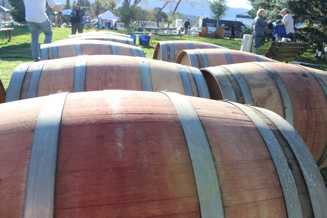 Rows of wine barrels outside, people in background.