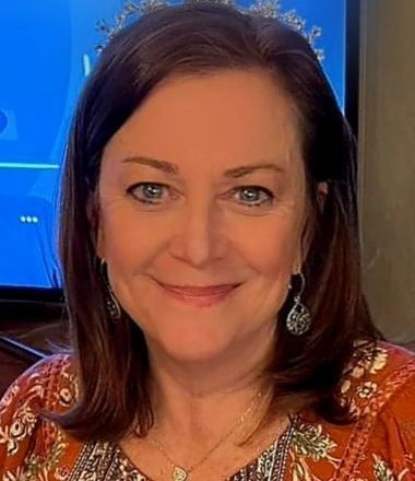 Woman with brown hair, blue eyes, wearing orange top, smiling.