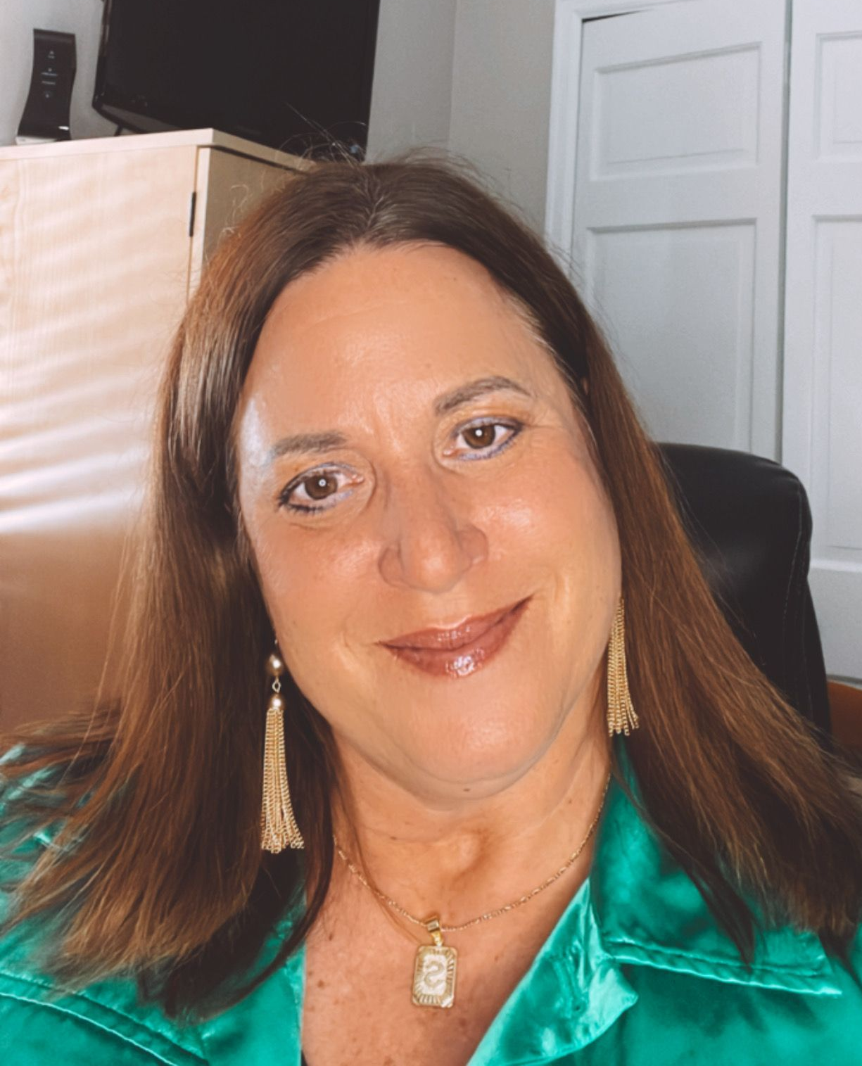 Woman with brown hair, smiling, wearing green shirt and long earrings.
