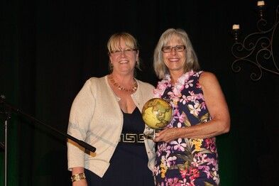 Two women smiling, one holding a globe award on a stage.