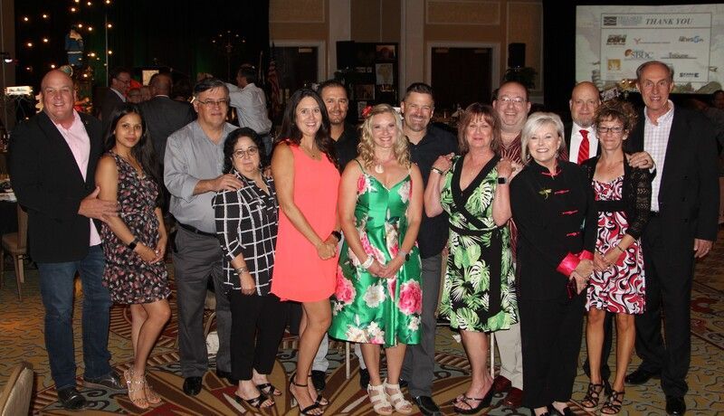 Group of people smiling at a gala event, diverse ages and attire, posing for a photo.