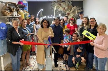 People at a ribbon-cutting ceremony for a store, with a woman cutting the red ribbon.