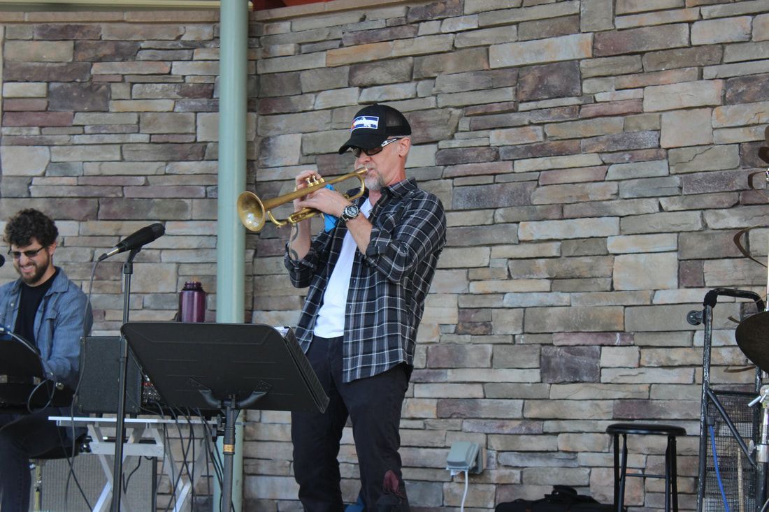 Man playing trumpet on stage in front of a stone wall; another man plays a keyboard.