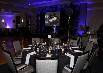 Formal event setting with round tables, black tablecloths, place settings, and stage in background.