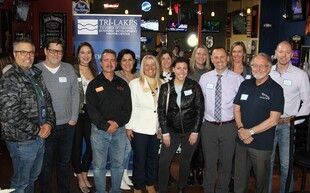 Group of people posing for a photo at a bar, with banner for 'Treelakes'.