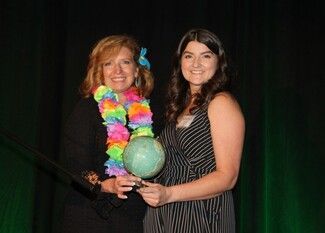 Two women on stage holding a globe award; one wears a lei, the other a striped dress.