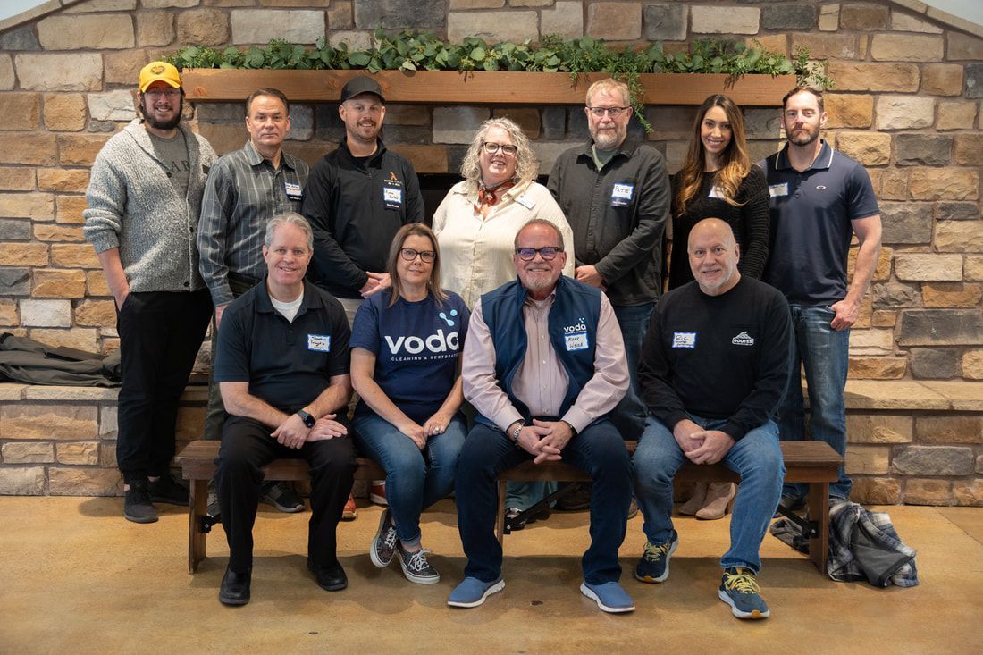 Group of people posing in front of a stone fireplace. Some are sitting, some standing, all wearing name tags.