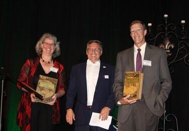 Three people holding awards on a stage, two are smiling.