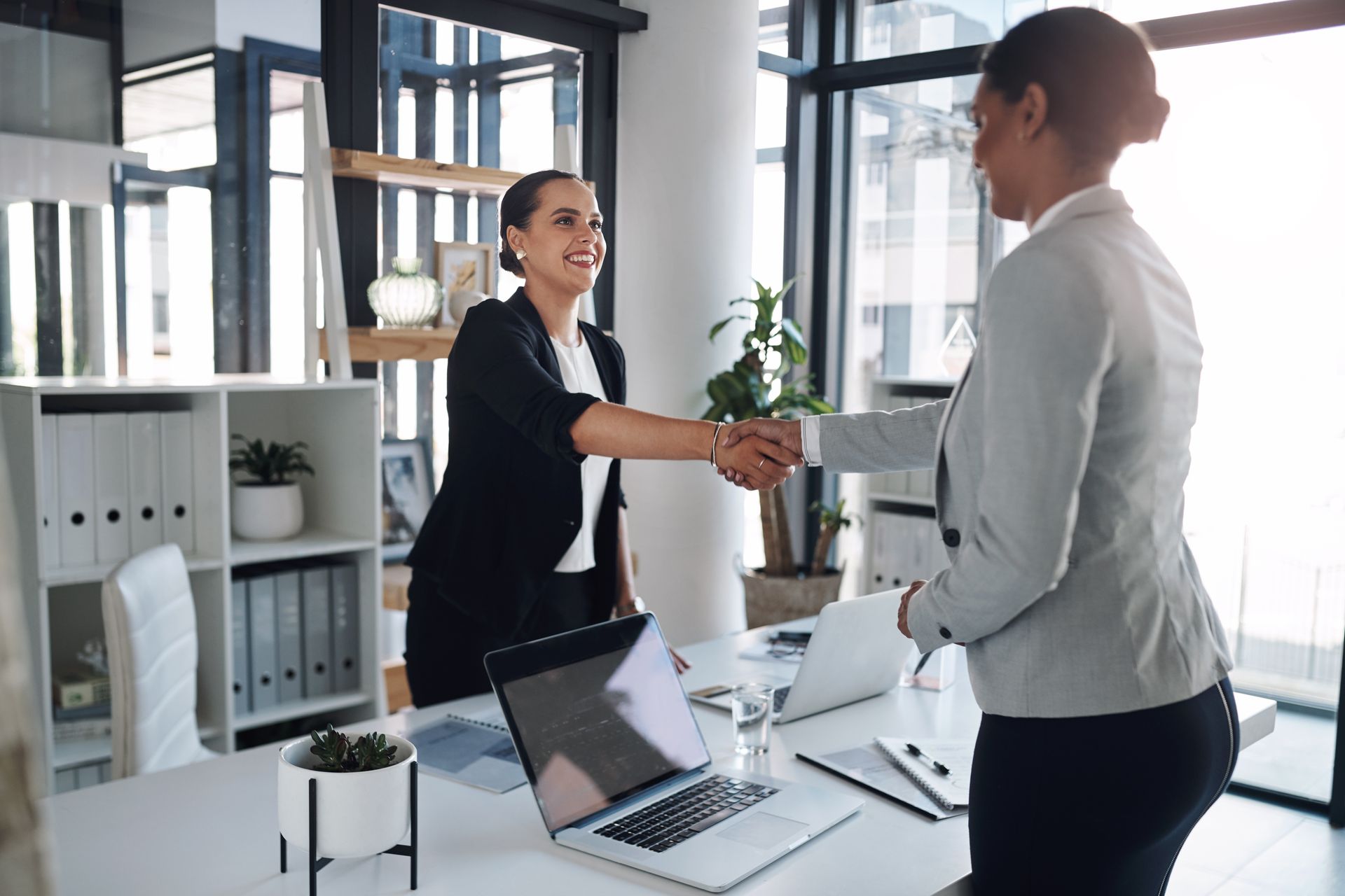 Two women are shaking hands in an office.