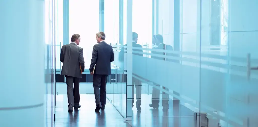 Two men in suits are walking down a hallway in an office building.