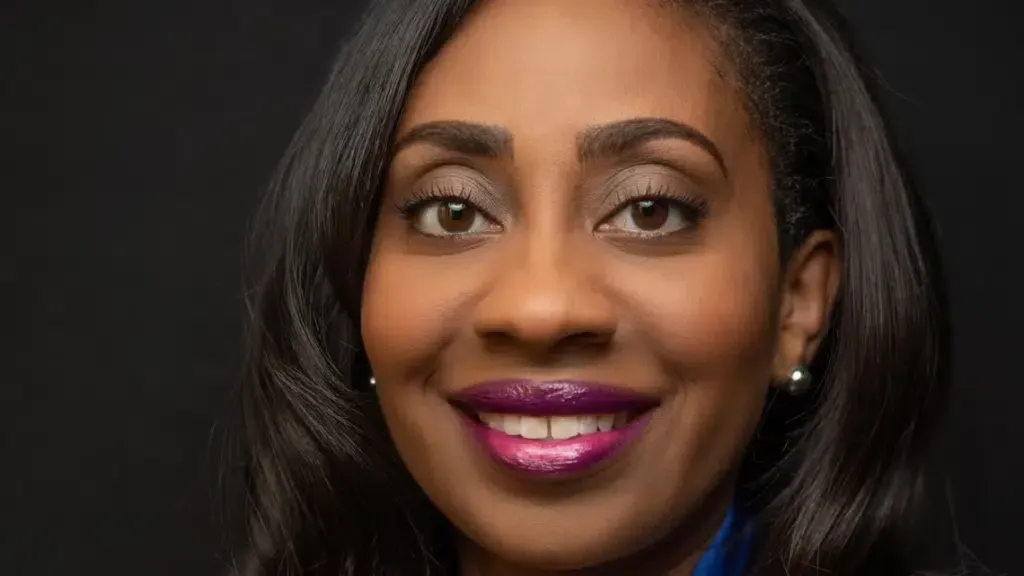 A woman with purple lipstick and earrings is smiling for the camera.