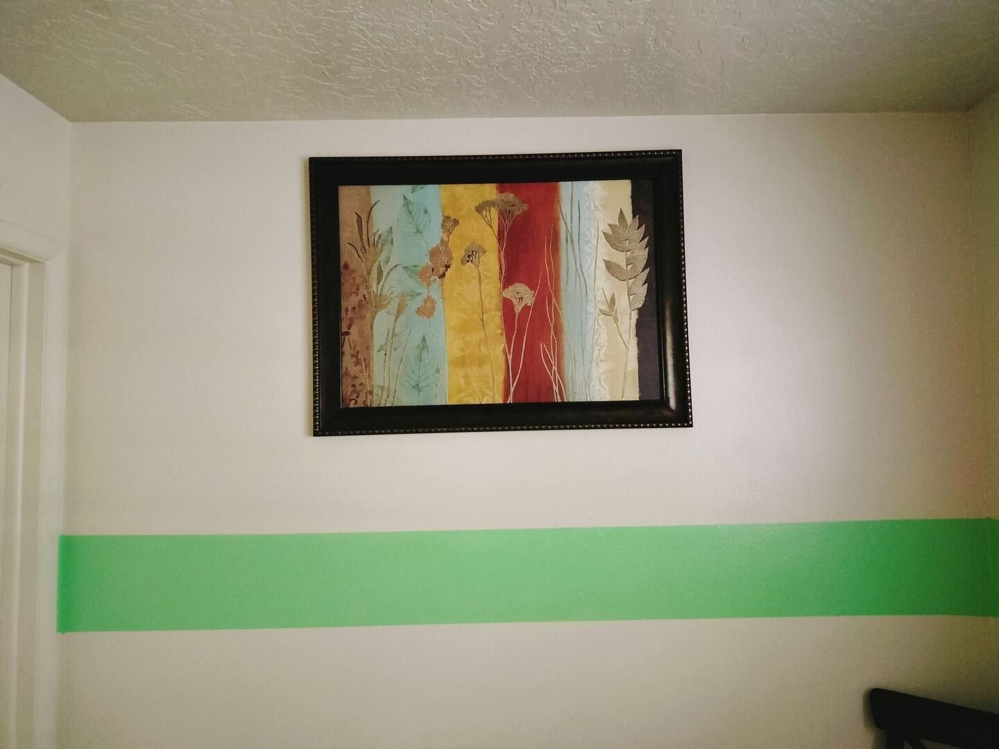 A framed picture hangs on a white wall next to a green stripe