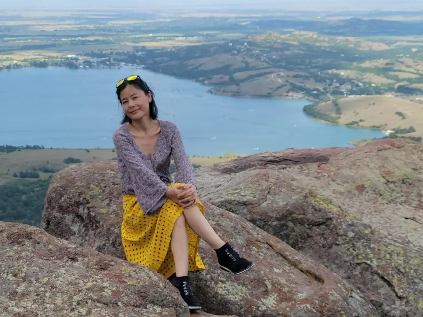 A woman is sitting on top of a rock overlooking a lake.