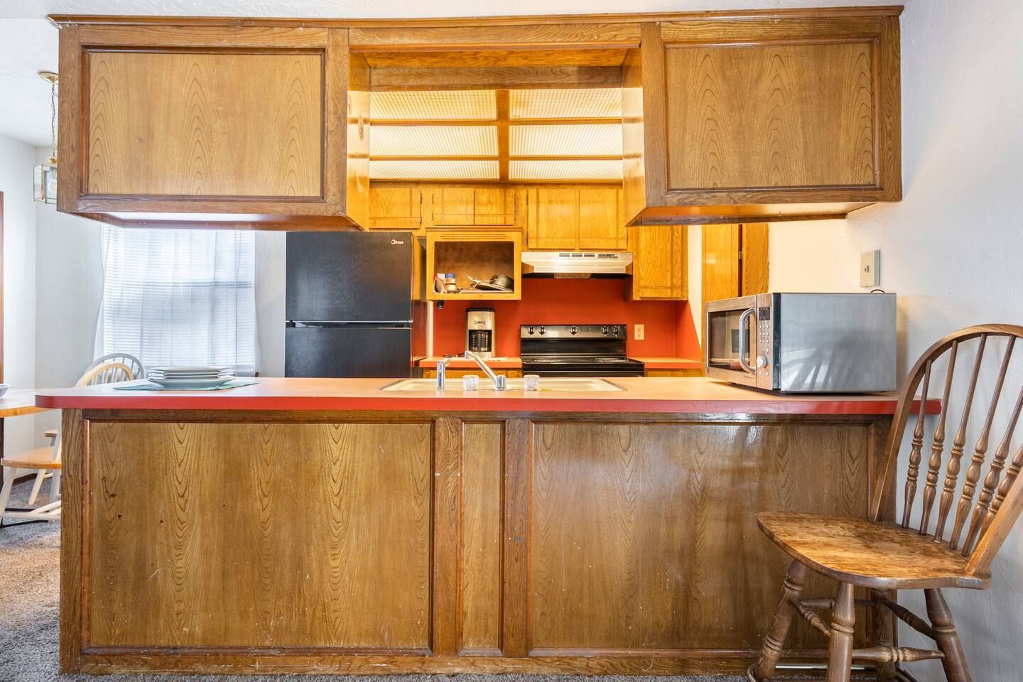 A kitchen with wooden cabinets , a black refrigerator , a microwave , a sink , and a chair.