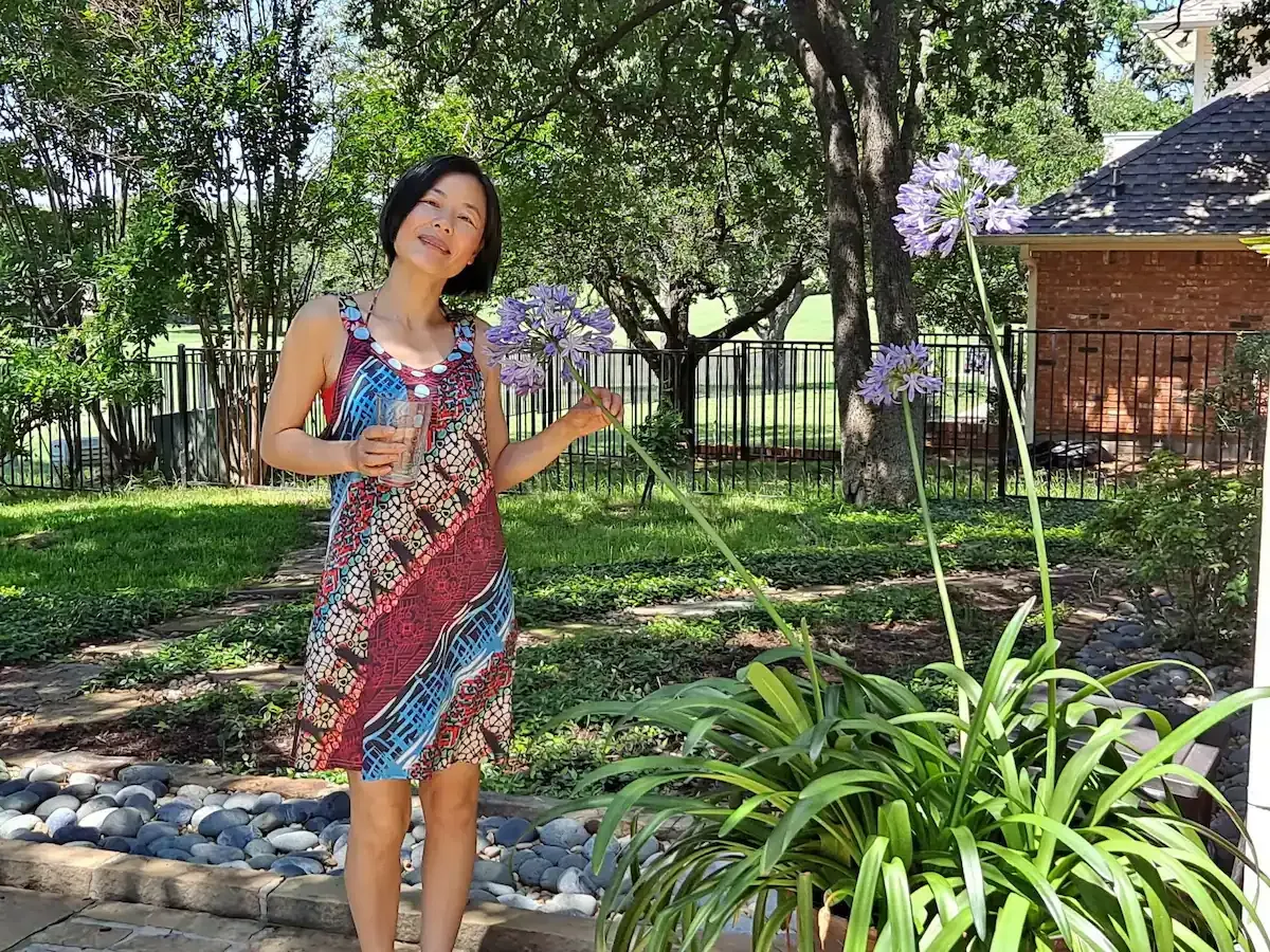 A woman in a dress is standing next to a plant with purple flowers.