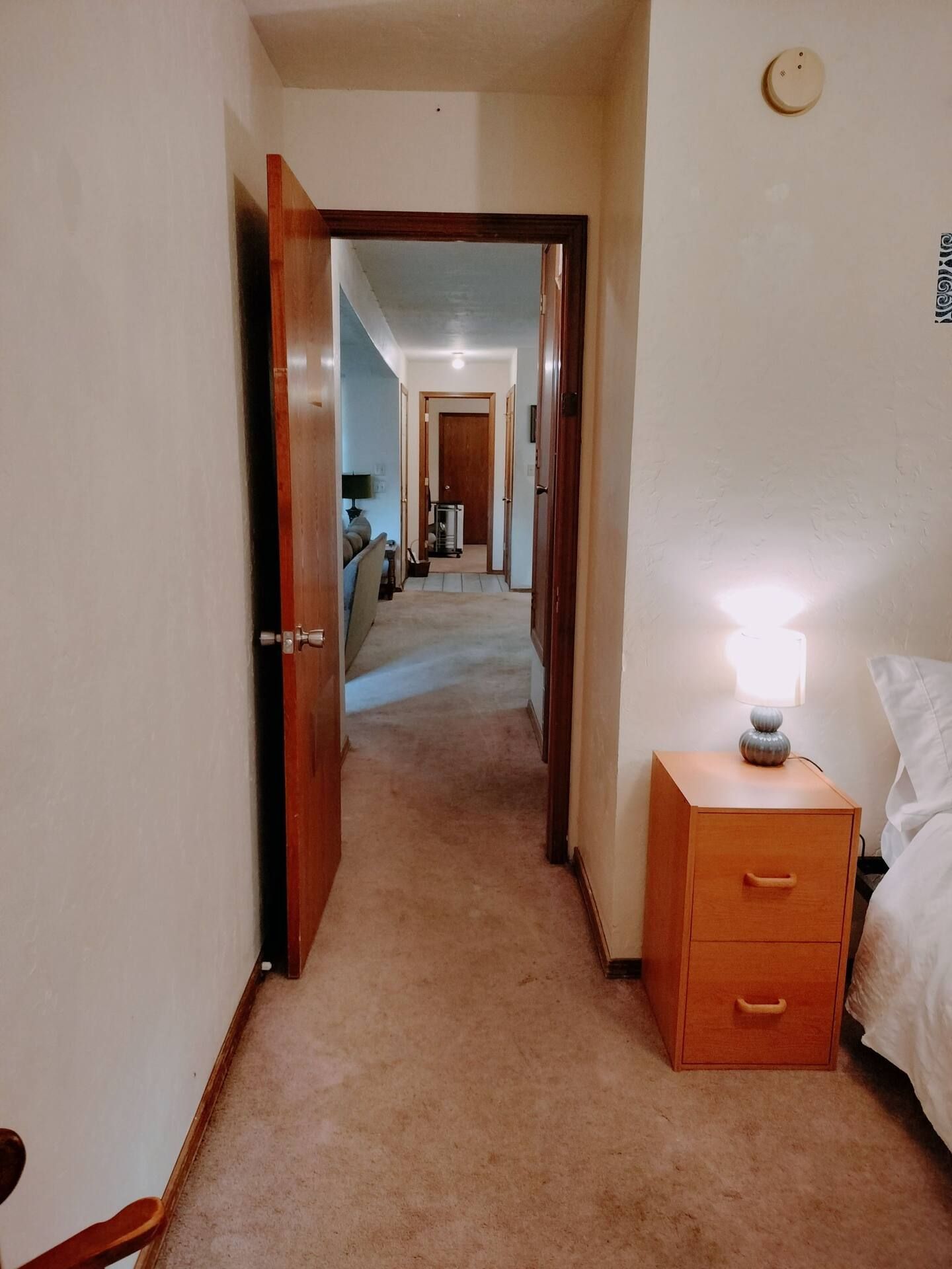 A hallway leading to a bedroom with a bed and nightstand