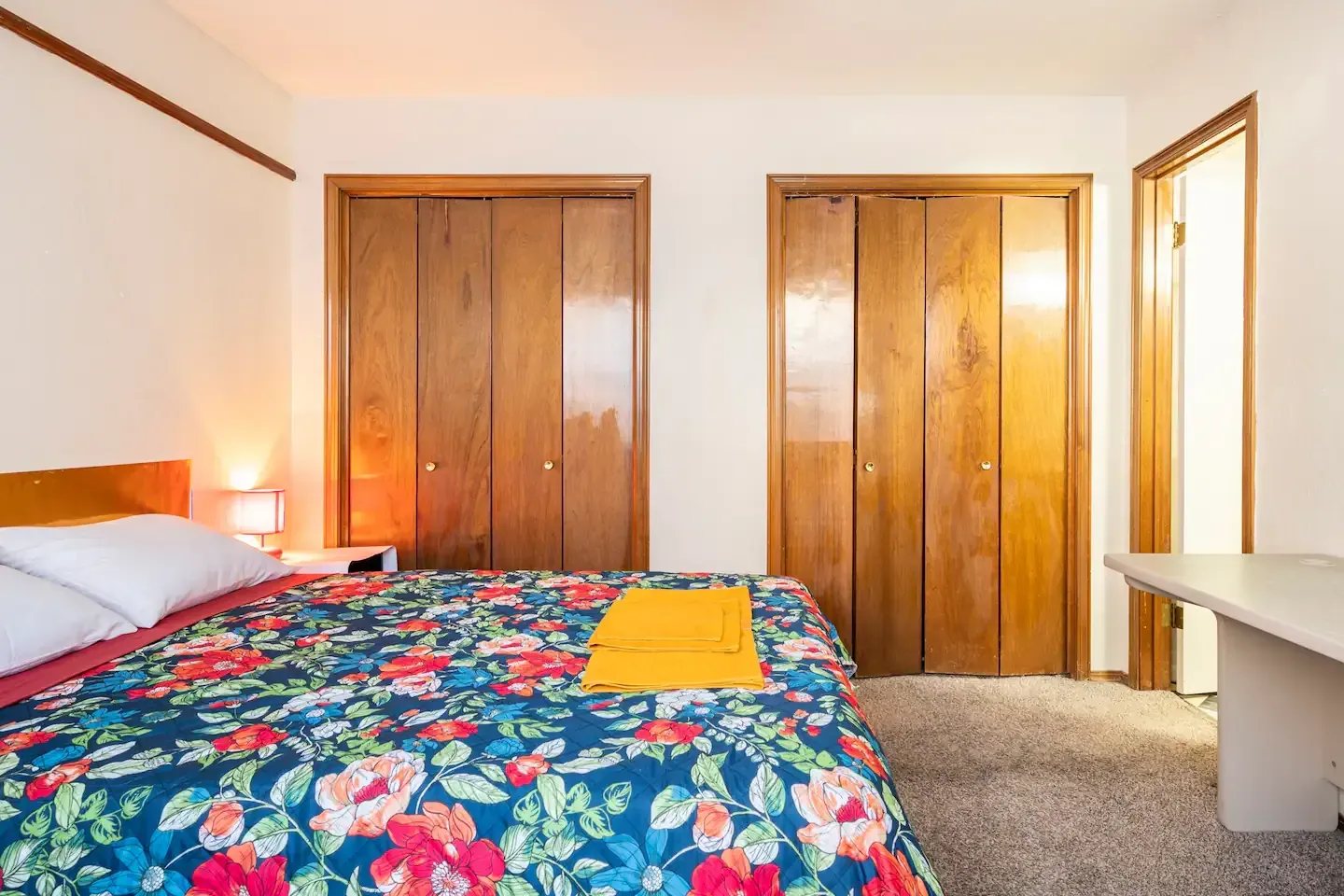 A bedroom with a bed , closets and a bench.