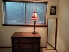 A bedroom with a dresser , lamp , mirror and window.