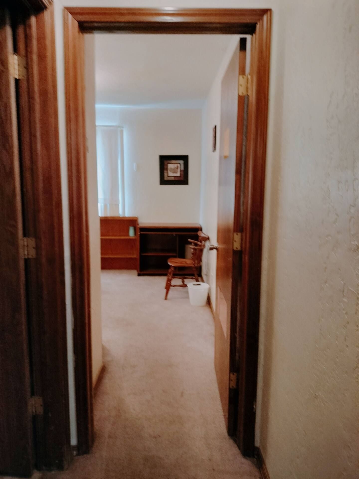 A hallway leading to a bedroom with a chair and a desk.
