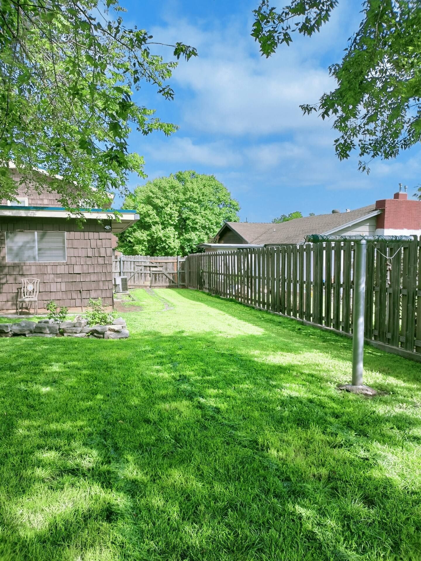 A lush green backyard with a wooden fence and a house in the background.