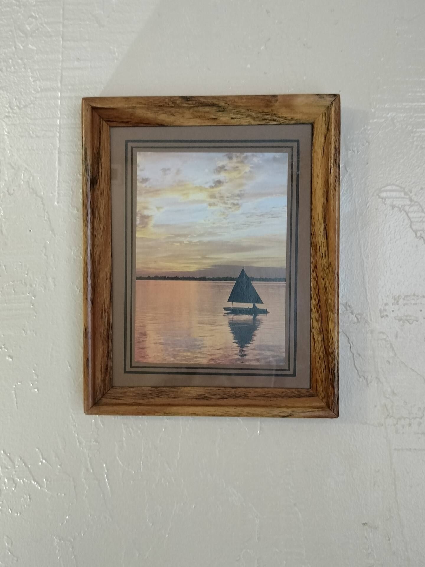 A painting of a sailboat in the water is hanging on a wall.