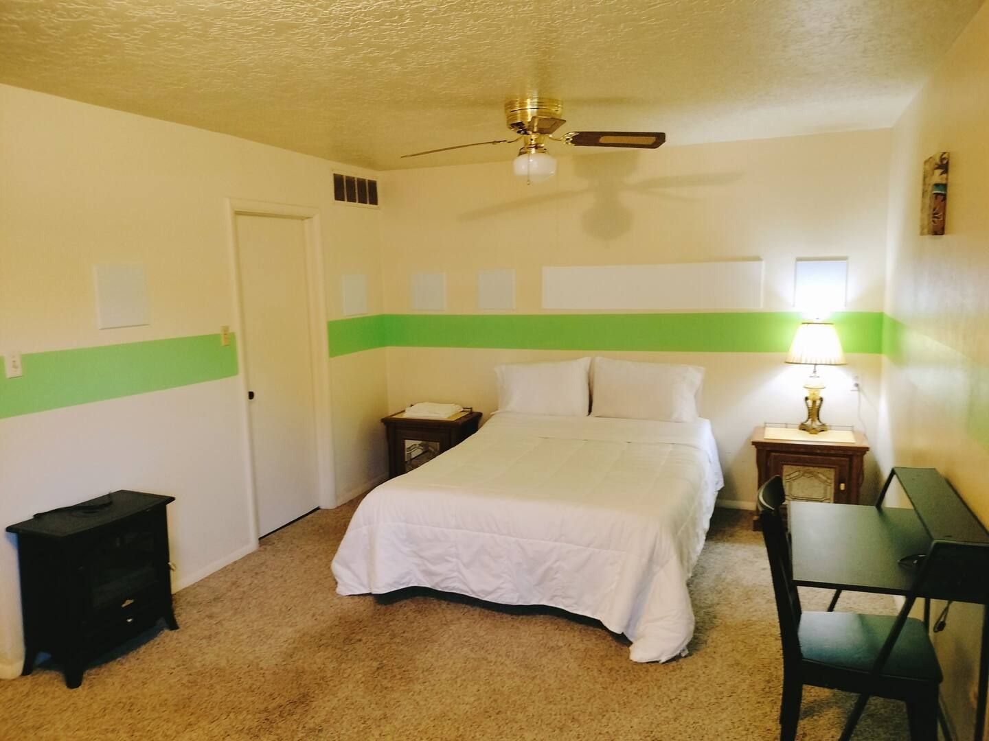 A bedroom with a bed a desk and a ceiling fan