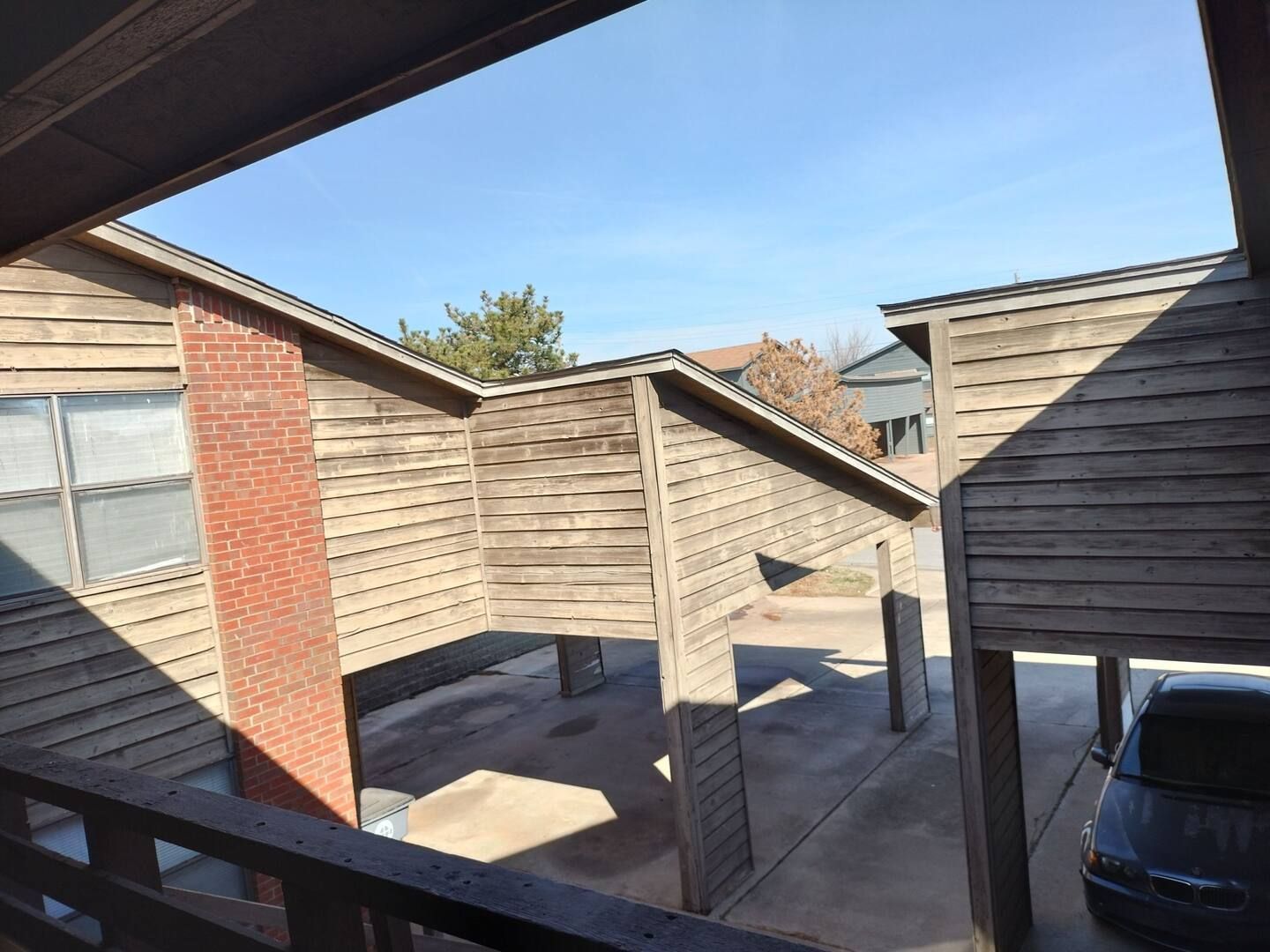 A car is parked under a wooden structure in a parking lot