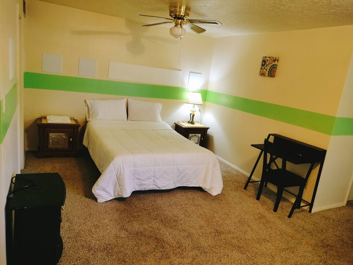 A bedroom with a bed a desk and a ceiling fan