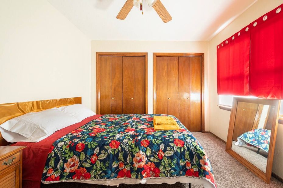 A bedroom with a bed , a mirror , a ceiling fan and red curtains.