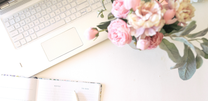 Pastel laptop and pink flowers on a bright desk with notebook and planner