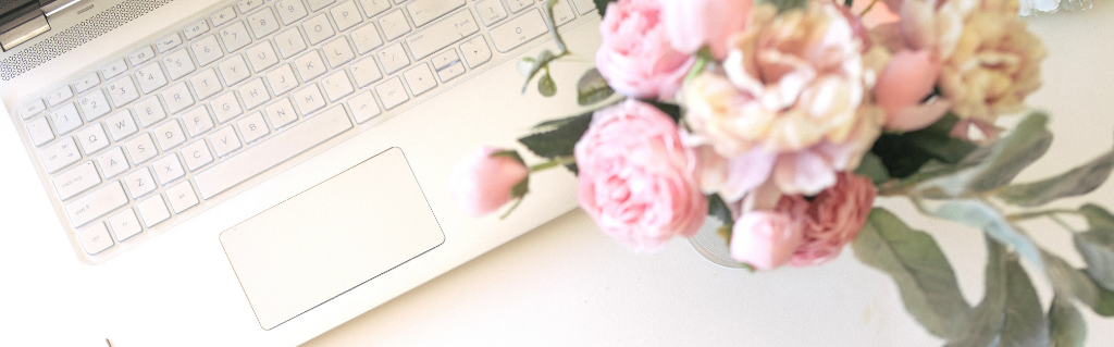 White laptop keyboard beside pink flowers on a light desk