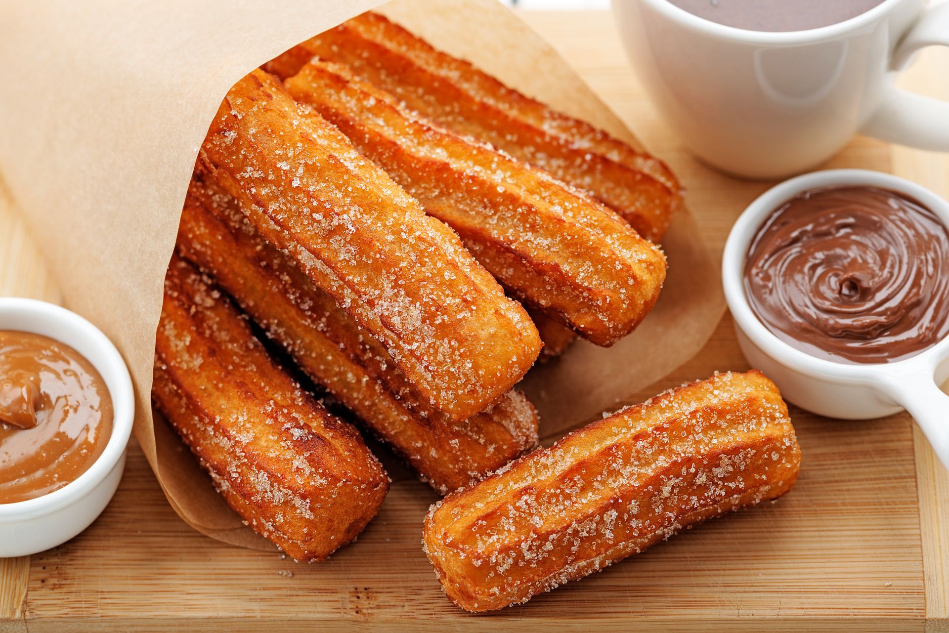 Golden churros dusted with sugar, served with chocolate and caramel dips, and a cup of hot chocolate.