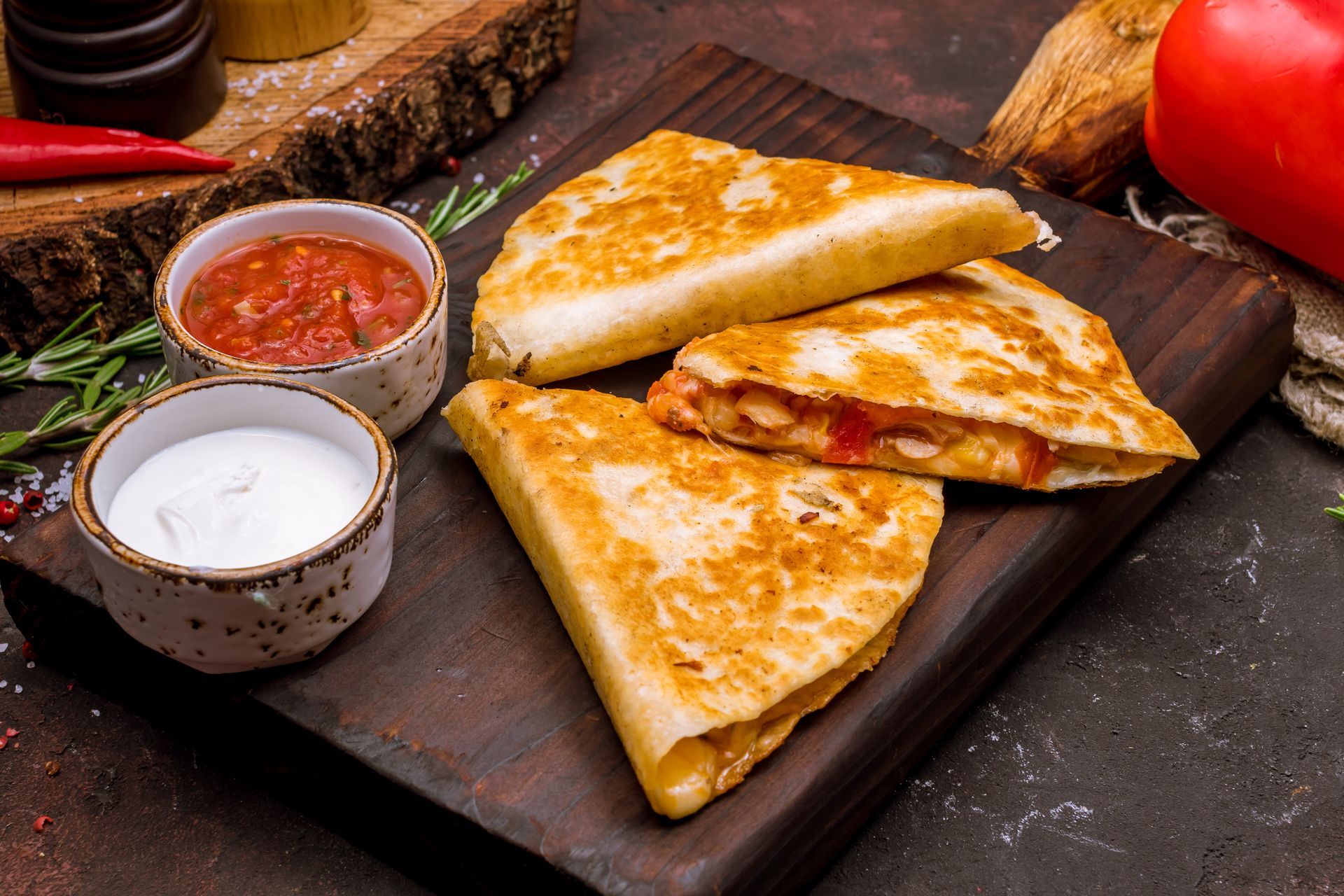 Quesadillas on a wooden board with dipping sauces; salsa and sour cream.