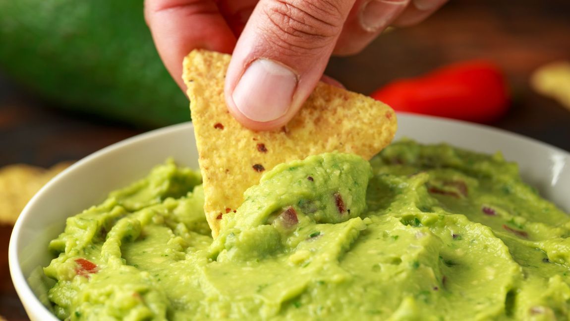 Hand dipping a tortilla chip into creamy green guacamole. Hand dipping a tortilla chip into creamy green guacamole.