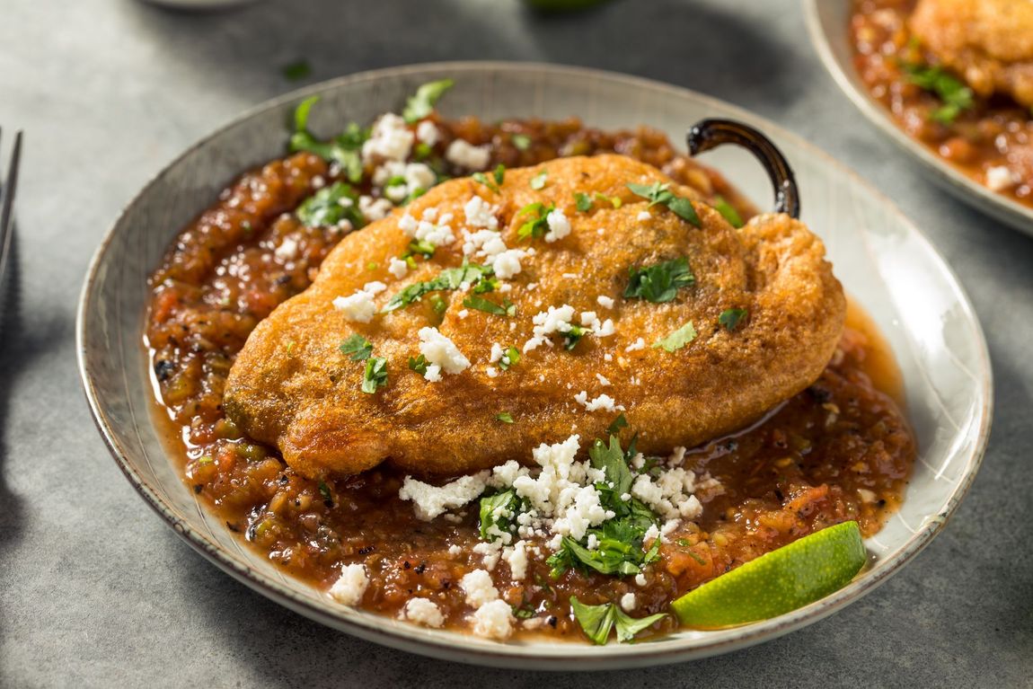 Chile relleno with salsa, garnished with cheese, cilantro, and lime on a plate. Chile relleno with salsa, garnished with cheese, cilantro, and lime on a plate.