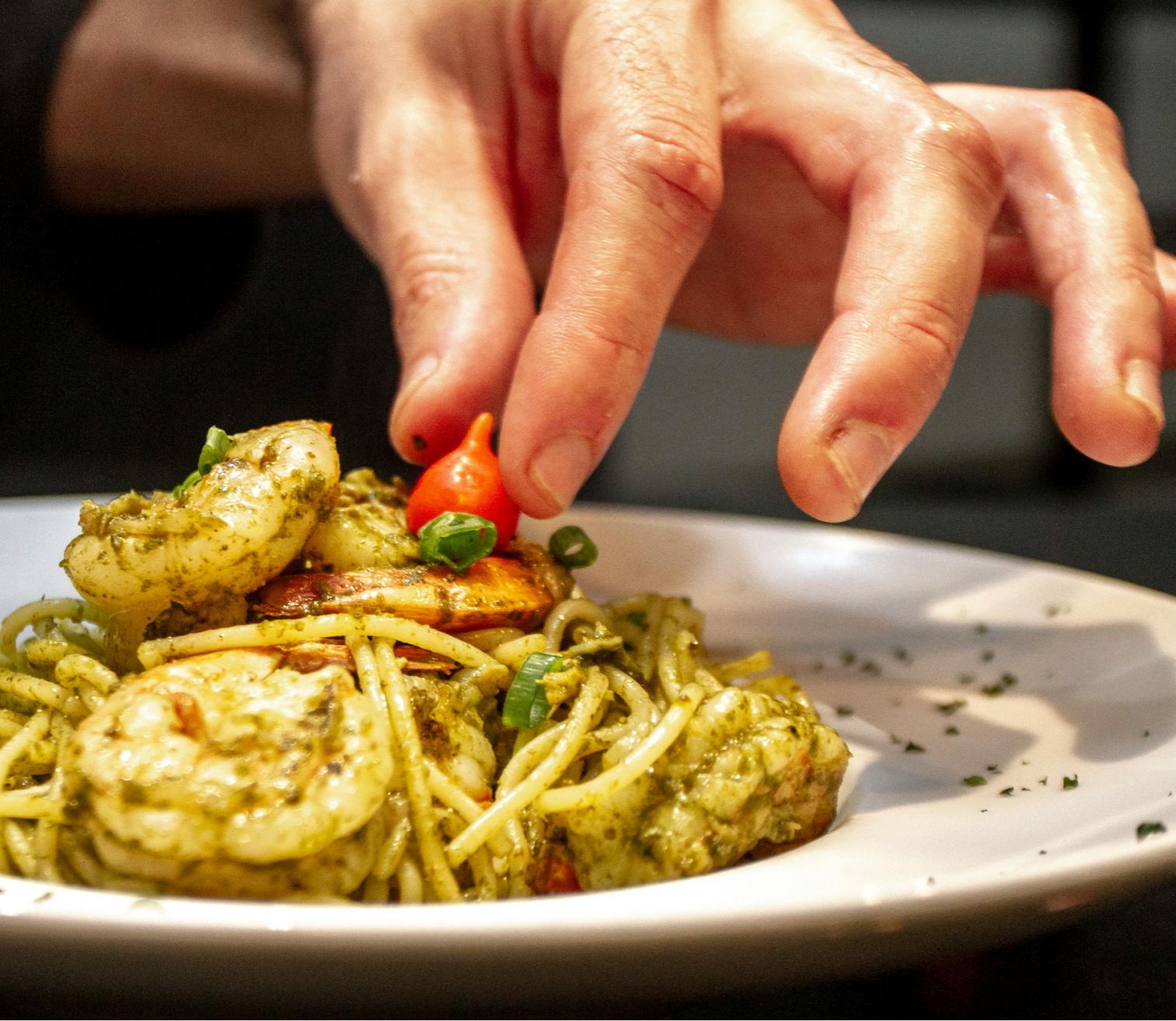 A person is putting a tomato on top of a plate of spaghetti