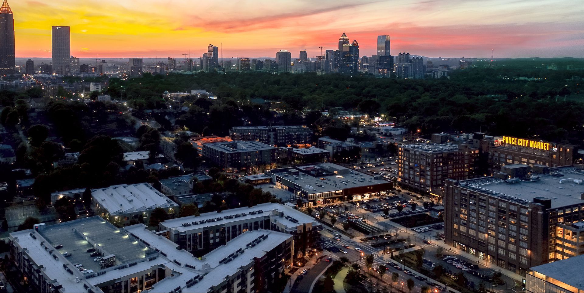 An aerial view of a city at sunset with a skyline in the background.
