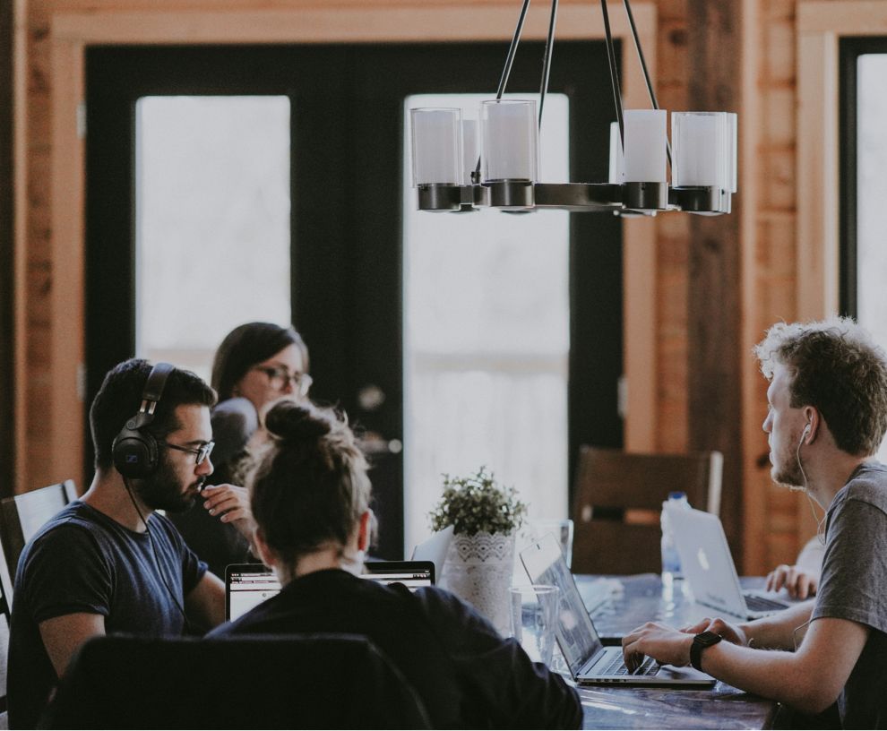 A group of people are sitting around a table with laptops.