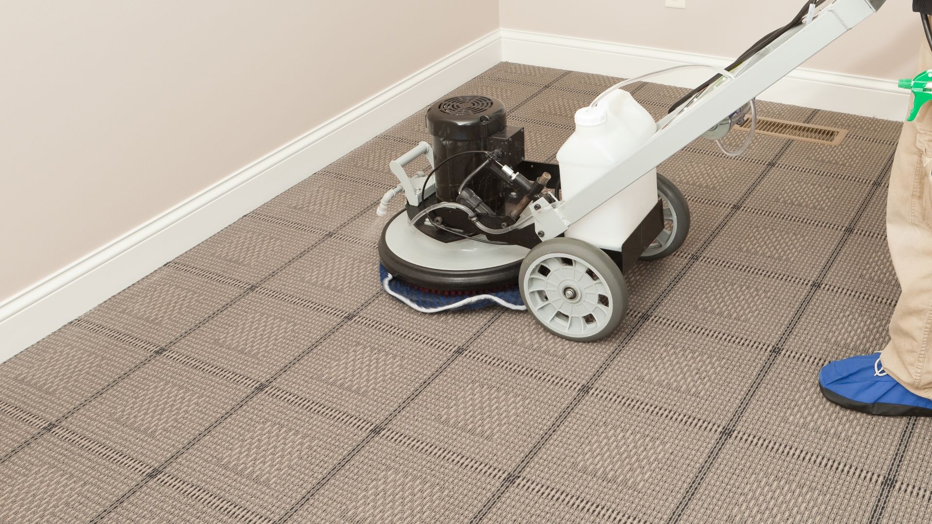 Carpet-cleaning machine on patterned carpet beside a wall, with a person’s blue shoe partly visible.