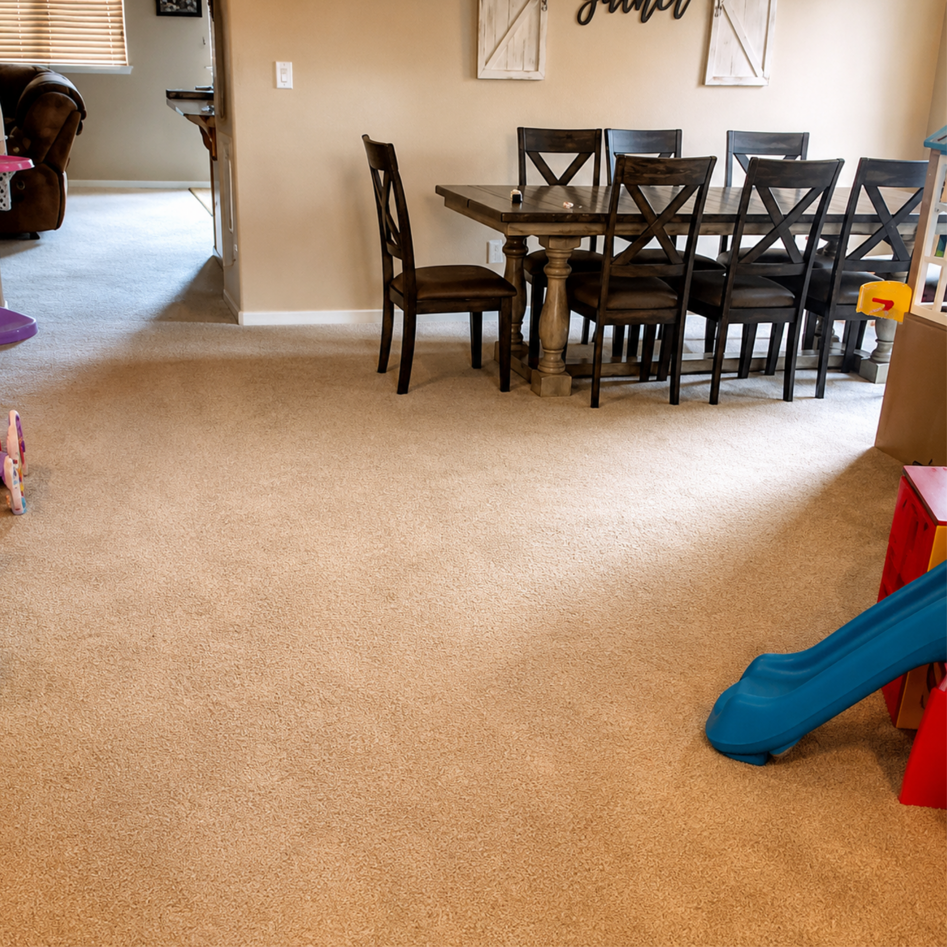 Carpeted living room with dining table and chairs, blue slide on the right, and toys near the doorway.