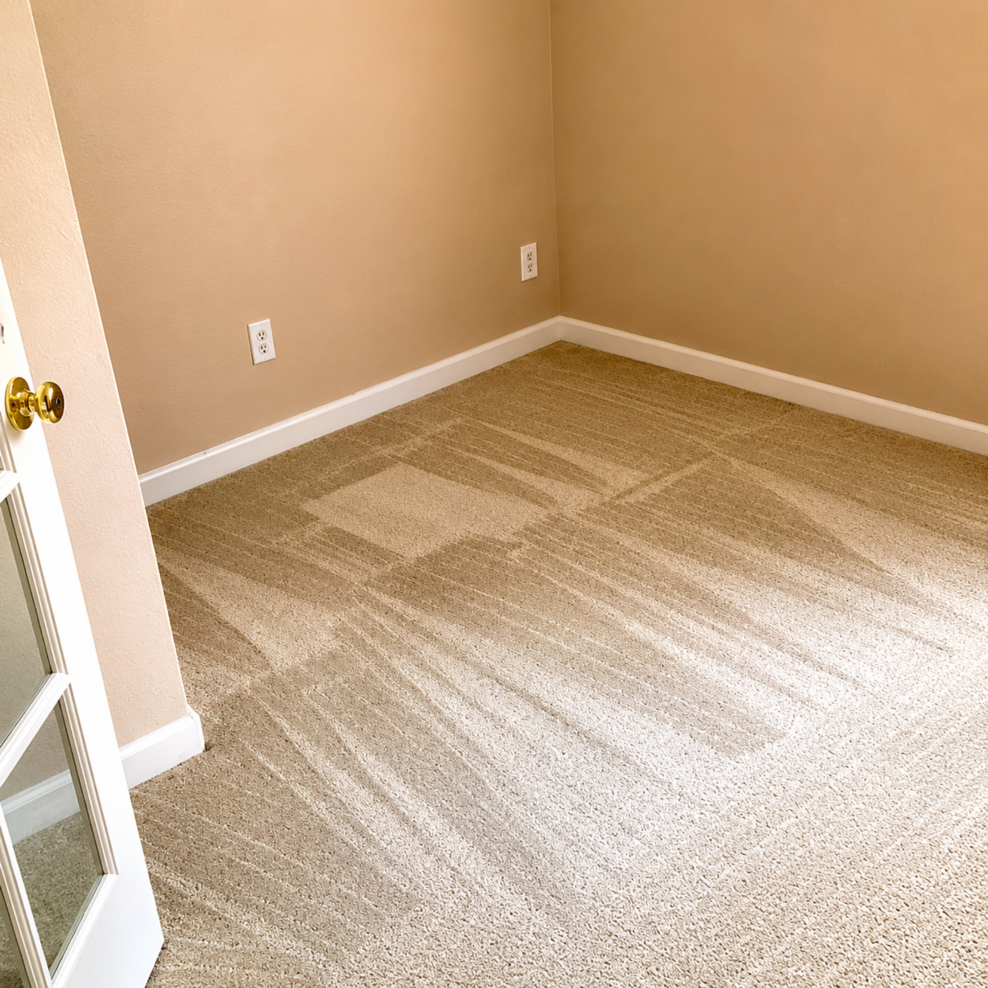 Empty beige carpeted room with tan walls and white trim, viewed from the doorway.