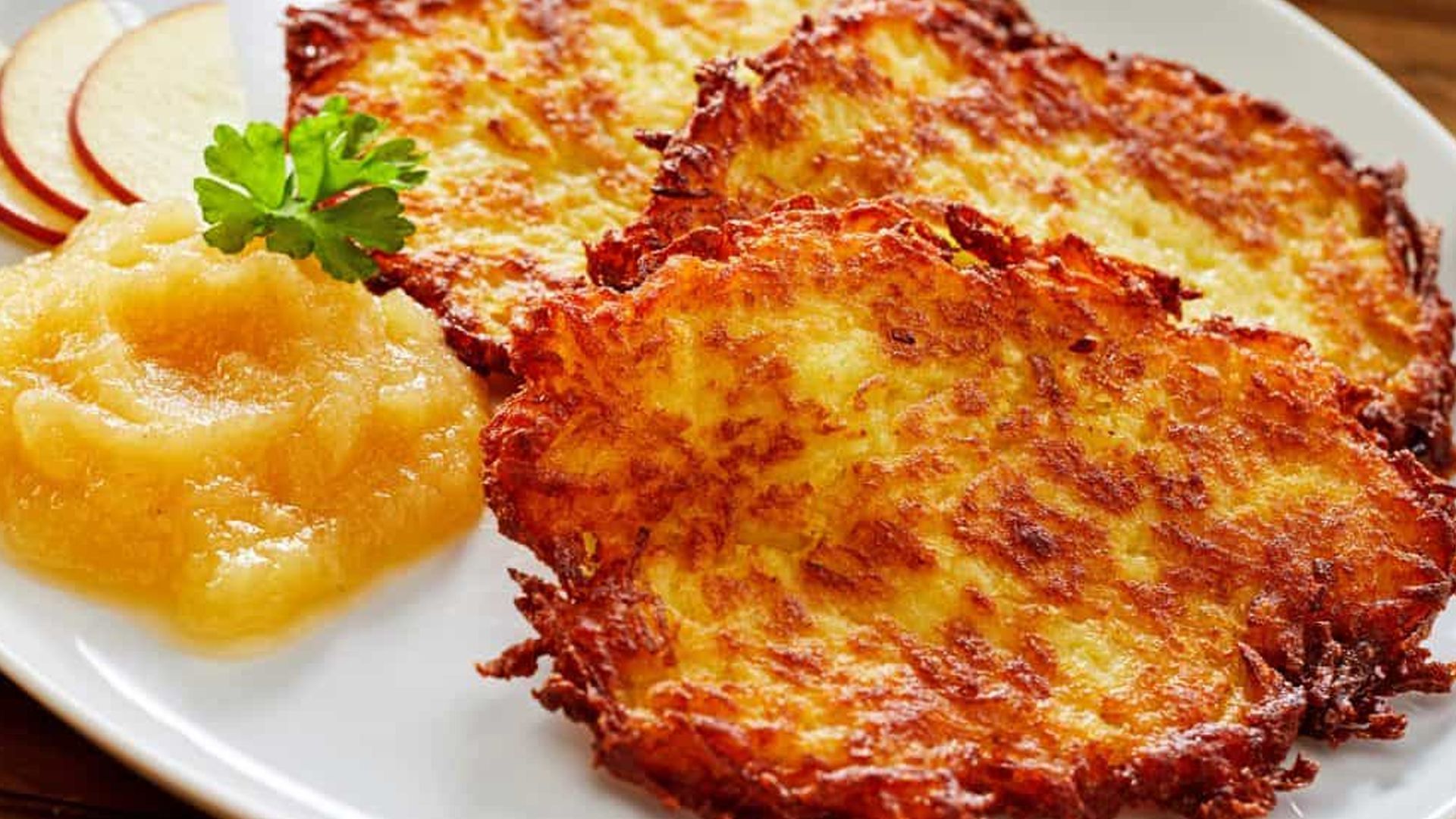A white plate topped with potato pancakes and applesauce.