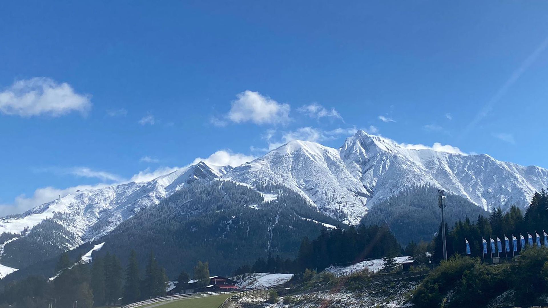 A snowy mountain range with trees in the foreground and a blue sky in the background