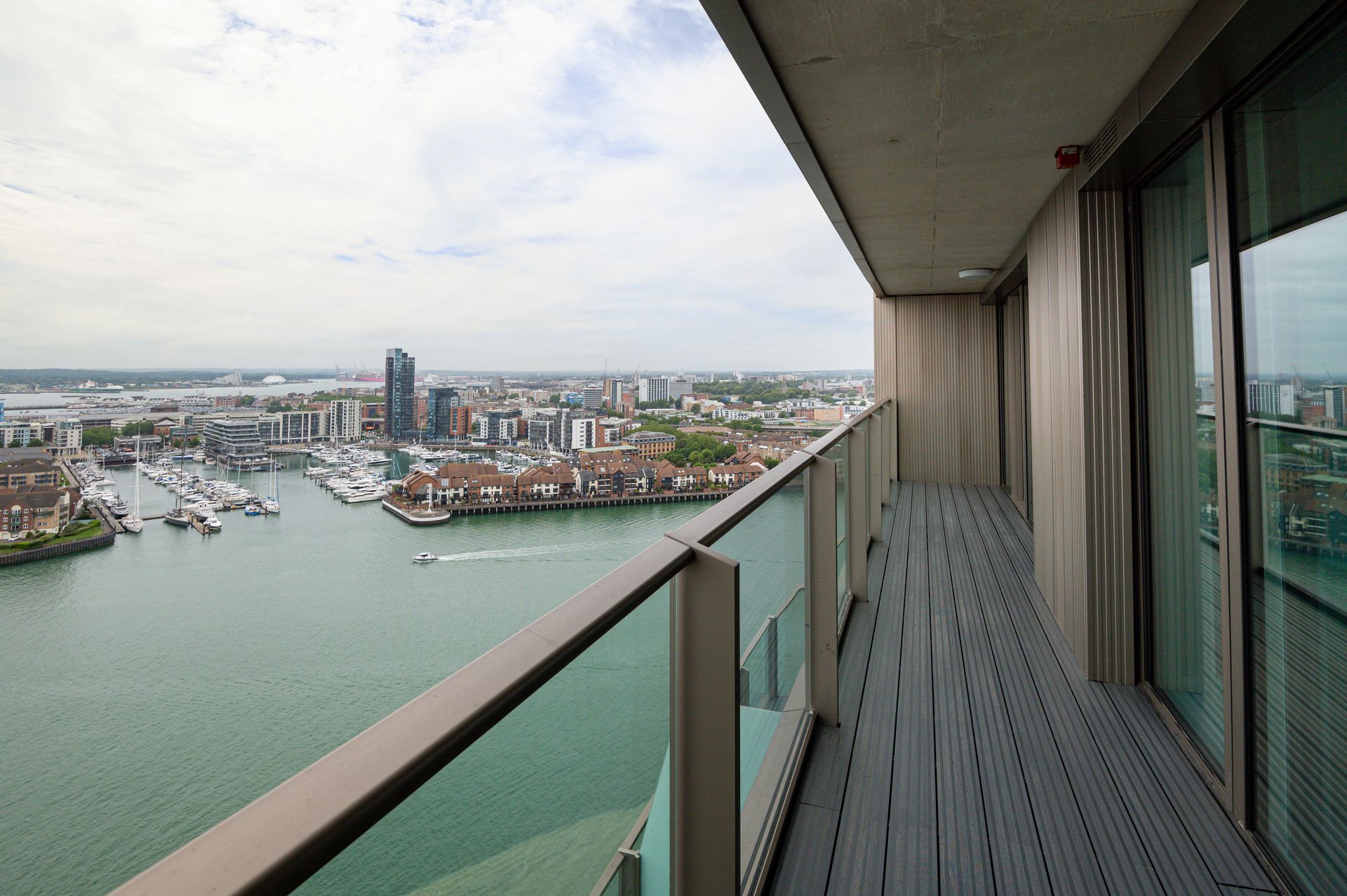 High-rise balcony overlooking a harbor and city skyline under a cloudy sky
