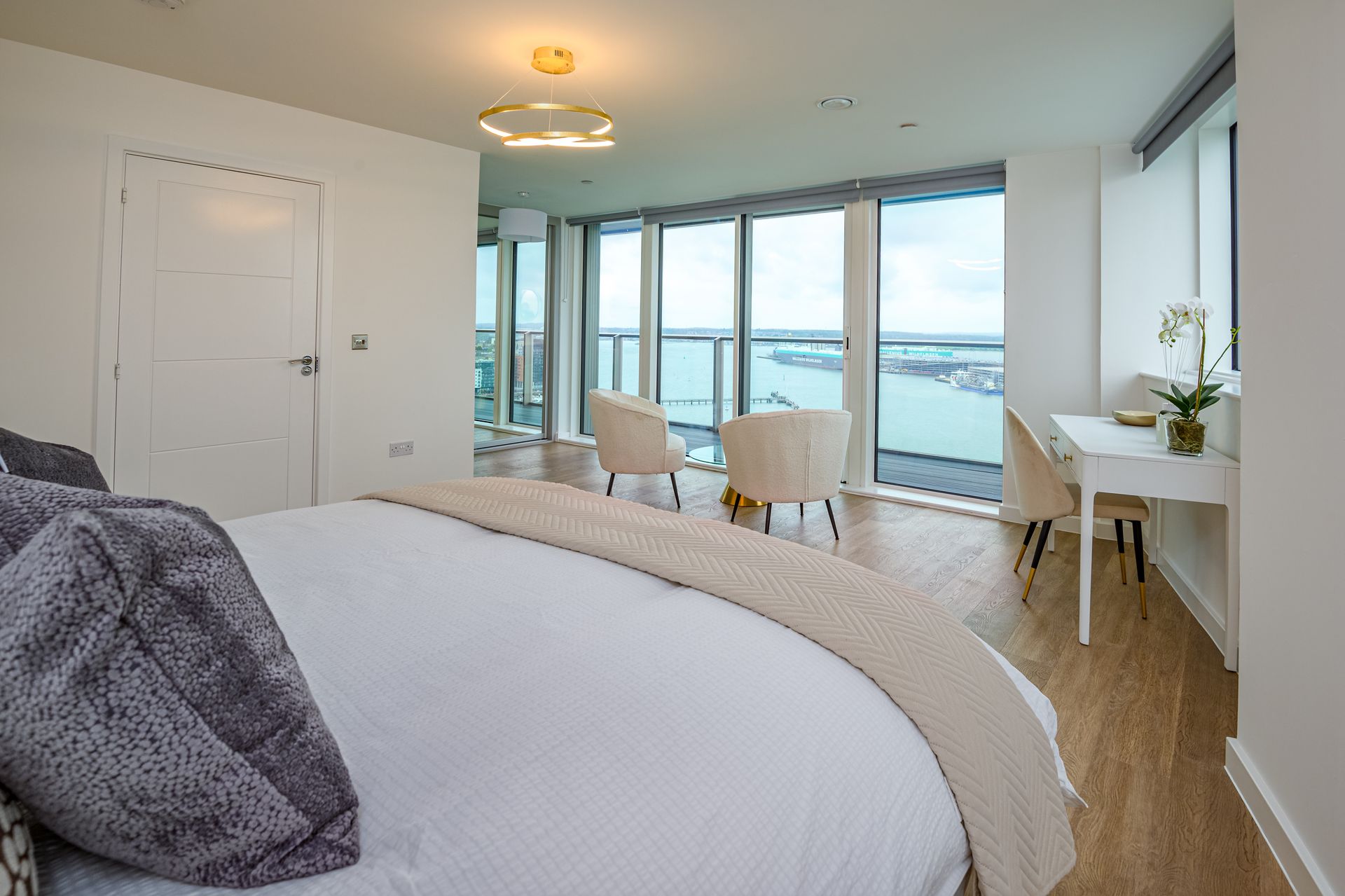 Bright bedroom with large windows, sea view, white furniture, and a bed in the foreground